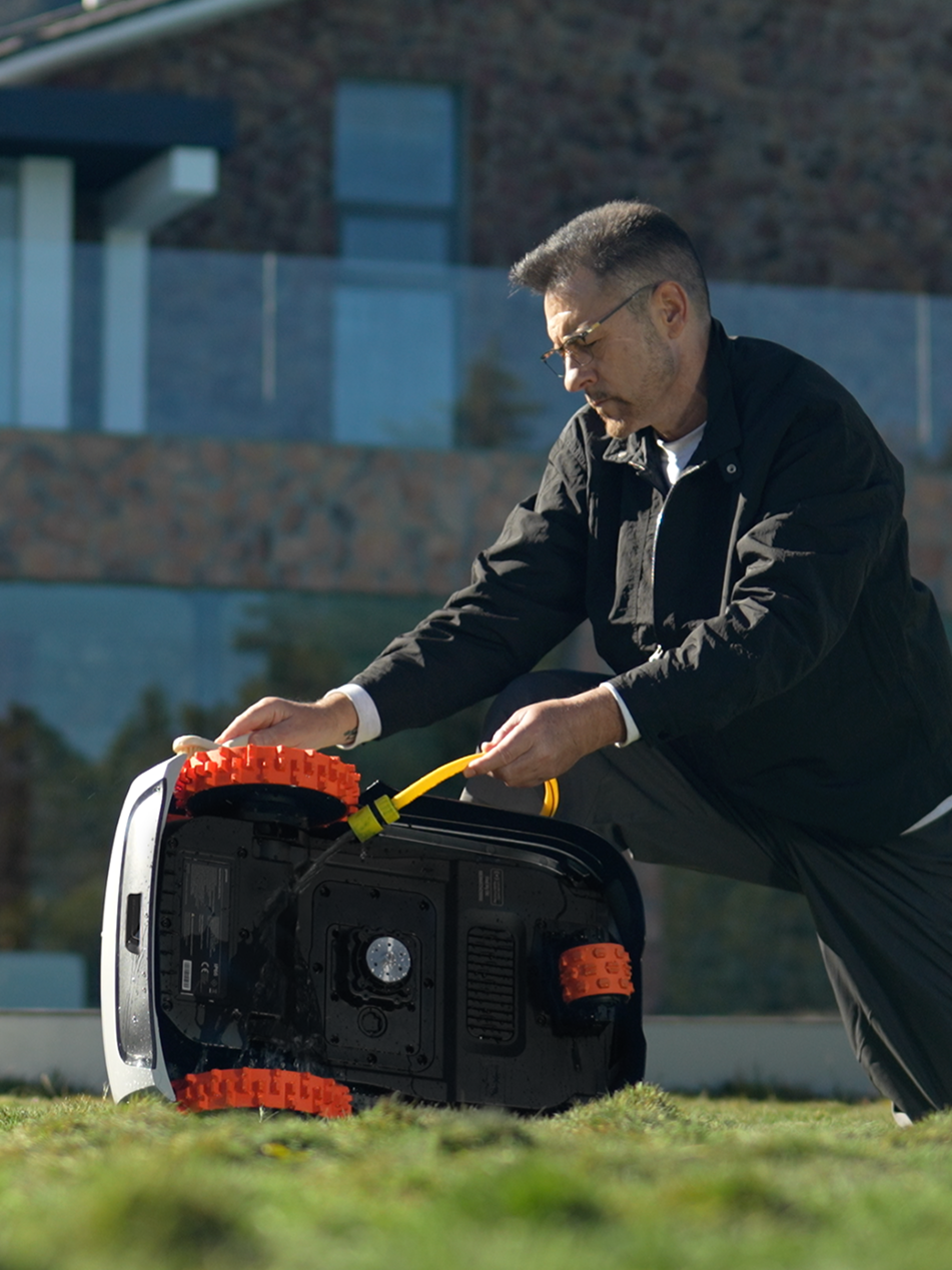 Man cleaning Segway Navimow i105E robot lawn mower in garden.